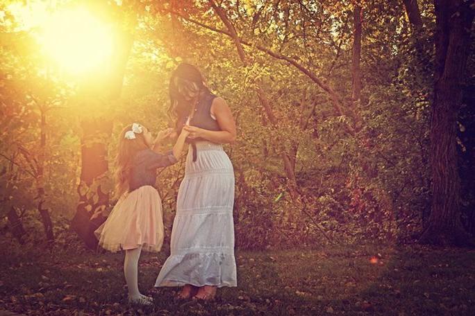 一个小女孩在树林里抬头看着她的母亲，夕阳透过树林洒下金色的光芒